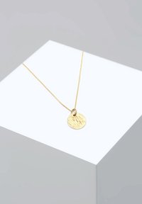 Zlatý náhrdelník s príveskom v tvare textúrovaného kruhu na jemnom reťazci, zobrazený na minimalistickom svetlom pozadí.