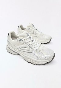 Baskets blanches de sport avec des panneaux en mesh et synthétiques, lacets noués, et des accents gris sur les semelles et les talons, positionnées sur un fond blanc.