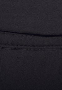 Der schwarze Stoff weist eine glatte Textur auf und hat eine Nahtdetails entlang der oberen Kante, die ein mehrschichtiges Aussehen kreiert.