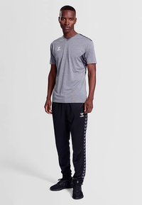 Grå atletisk T-shirt med V-hals og korte ærmer, kombineret med sorte træningsbukser med sidestriber og logo. Tekstureret stof, sporty design.