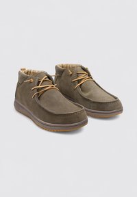 Zapatos de ante verde olivo con puntera redonda, cordones en color marrón claro y un forro interior con patrón. Suela de goma flexible con agarre texturizado.
