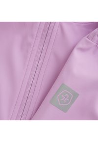 Ljuslila jacka med en slät textur. Har en central dragkedja, elastiska ärmslut och ett logotypmärke i ljusgrått på ärmen.
