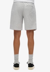 Pantalones cortos de algodón gris con un corte relajado, que cuentan con un bolsillo trasero y bordes dobladillados, combinados con zapatos negros y calcetines gris claro.