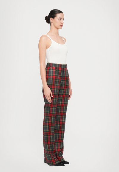 Red and green plaid trousers with a straight-leg design, high waist, and pockets, paired with a fitted white tank top and black heels.