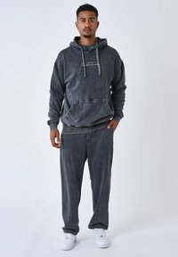 Sudadera de algodón gris con un bolsillo frontal y cordón ajustable, combinada con pantalones de chándal a juego. Ambas piezas presentan una textura suave y desgastada.