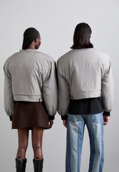 Grå pufferjackor med överdimensionerade axlar, kort längd och ribbade ärmar, bärs över en brun kjol och tv�åtonade jeans.