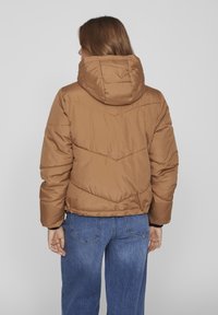 Brun puffy bomberjacka med huva, med ett quiltat mönster och kort design, parat med blå denimjeans.