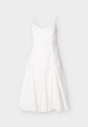 Λευκό μίντι φόρεμα χωρίς μανίκια με λεπτές τιράντες στους ώμους και φούστα που ανοίγει, παρουσιασμένο σε απλό ανοιχτό φόντο.