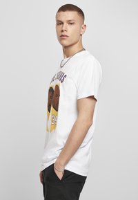 Hvid bomulds t-shirt med to illustrerede ansigtstræk, "34" grafik og lilla tekst på fronten. Kortærmet, afslappet pasform.