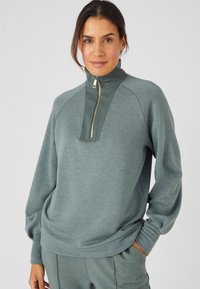 Pullover verde chiaro con colletto alto, zip frontale e dettagli a coste. Realizzato in morbido tessuto testurizzato, con maniche lunghe e vestibilità rilassata.