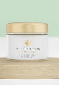 Ein klarer Glasbehälter mit einem goldenen Deckel, beschriftet mit "Age Perfection Skin Power Serie." Weißer Hintergrund, präsentiert ein minimalistisches Design und eine glatte Textur.