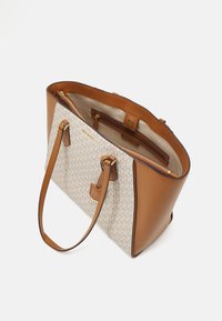Sac fourre-tout avec un corps en tissu beige arborant un motif discret, des accents en cuir tan, deux poignées et un compartiment zippé à l'intérieur.