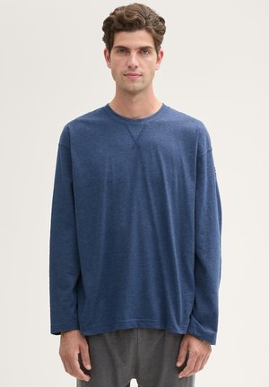 Langarmige blauwe t-shirt gemaakt van zachte stof. Met een ronde hals, een relaxte pasvorm en subtiele stikdetails. G gedragen met grijze broeken.