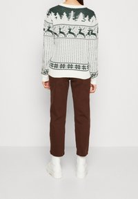 Vit tröja med grönt julmönster av renar och träd, i kombination med bruna byxor och vita ankelstövlar. Texturerad stickad design.