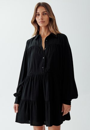 Black, button-up dress with long sleeves, tiered design, and textured fabric. Features a collar and subtle gathering at the bodice.