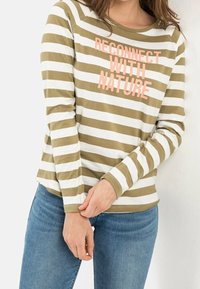 Femme portant un haut à manches longues beige et blanc rayé avec le texte « RECONNECT WITH NATURE », associé à un jean bleu.