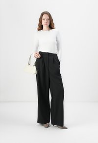 Black tailored wide-leg trousers, paired with a long-sleeve white top. Accessories include a small white handbag and nude high heels.