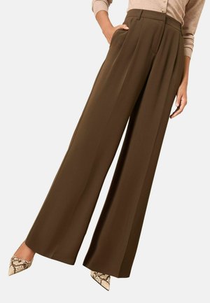 Hellebraune, weit geschnittene Hose aus glattem Stoff, mit vorderen Falten und Taschen, kombiniert mit spitzen Heels im Schlangenprint.