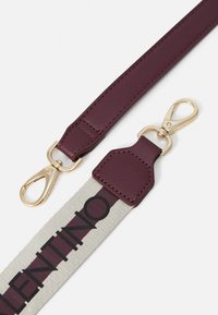 Bracelet en cuir bordeaux avec quincaillerie dorée et une partie en toile présentant des lettres noires, une finition texturée et des accents de couleur contrastante.
