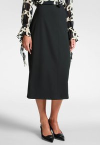 Musta midi-hame, joka on valmistettu sileästä kankaasta. Hameessa on istuva leikkaus, hienovaraiset sauma-otsikot ja se on yhdistetty kärjellisiin mustiin korkokenkiin.