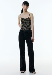 Schwarze Jeans im Schlagstil kombiniert mit einem braun-schwarzen Tierdruck-Top mit schmalen Trägern und ruffled Design.