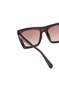 Ochelari de soare cu ramă din material țestoasă, cu formă unghiulară de ochi de pisică, lentile degrade de culoare maronie și brațe elegante cu detalii ale logo-ului.