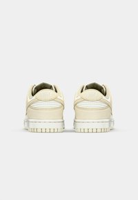 Nike Sneaker mit einem Obermaterial aus beigem Wildleder und Leder, gepolstertem Kragen und weißer Gummisohle, mit Logo-Details auf der Rückseite.