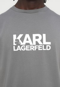 Szary t-shirt z krótkim rękawem z dużym białym napisem "KARL LAGERFELD" i sylwetkowym wzorem. Wykonany z miękkiej bawełny.