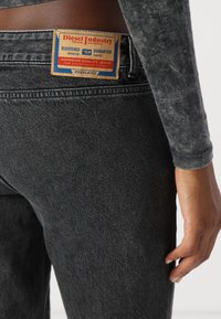 Jeans en denim noir avec une finition texturée, dotés d'une étiquette rectangulaire marron avec des détails rouges et bleus à l'arrière de la taille.