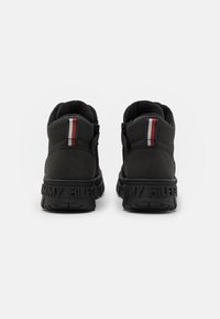 Czarne sneakersy o teksturowanym wykończeniu, z wyściełanym kołnierzem, czerwono-biało-niebieskim paskiem z tyłu oraz wytłoczonym logo "TOMMY HILFIGER" na podeszwie.