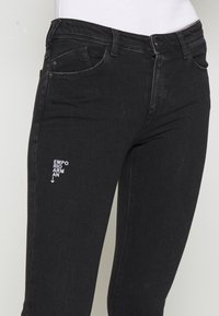 Mustat farkut, joissa on tiukka muotoilu, viisi taskua ja kirjailtu logo yksityiskohtana reidessä. Sujuva pinta ja klassinen leikkaus.