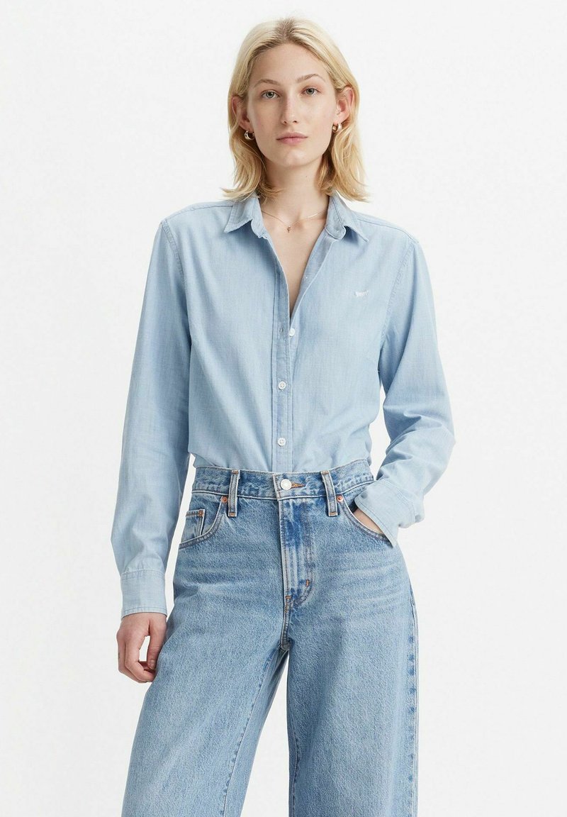 Lichtblauw overhemd met kraag, gemaakt van een zachte stof. Gecombineerd met hooggesneden, wijde blauwe jeans met contrasterende stiksels.