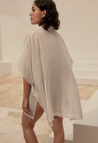 Lekkki, przezroczysty okrycie kimono w kolorze białym z pionowymi pasami, luźny krój i boczne rozcięcia dla swobody ruchu.