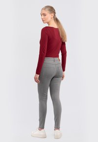 Red long-sleeve top with a slightly scooped back, paired with light gray fitted pants. White sneakers with thick soles complete the outfit.
