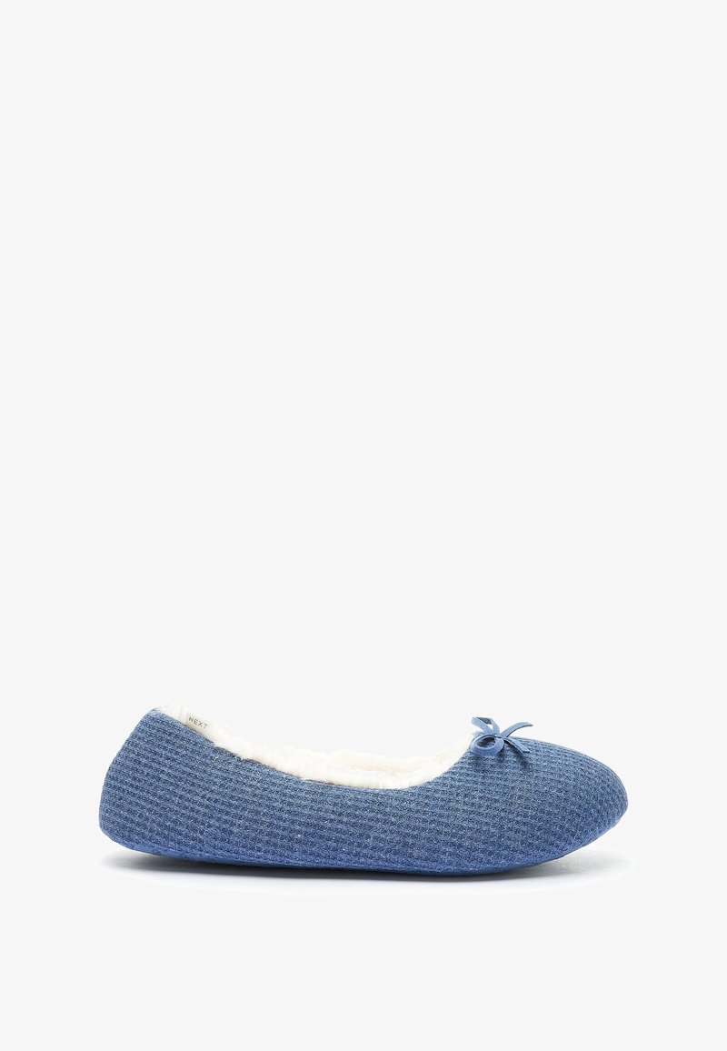 Pantoufle en tissu bleu avec un extérieur texturé, doublure en fausse fourrure blanche et un petit nœud décoratif sur l'orteil. Semelle plate, forme arrondie.