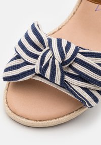 Navy och krämrandiga vävda sandaler med ett stort båtdetalj, kombinerat med en naturliknande espadrill-sula och en slät beige fotbädd.