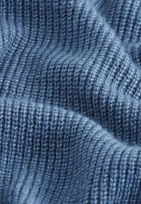 Primo piano di un morbido tessuto di maglia blu, con una texture visibile, un pattern a coste e pieghe delicate che creano ombre.