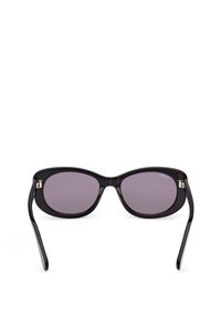 Sorte ovale solbriller med mørketonede linser og let buede stænger mod en hvid baggrund.