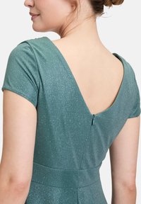 Robe teal à manches courtes, avec un dos en V profond et des paillettes subtiles. Dispose d'une fermeture éclair et d'une taille cintrée pour mettre en valeur la silhouette.