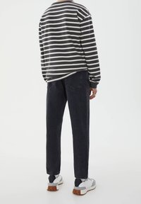 Camisa de manga larga a rayas en gris y blanco roto, combinada con jeans de mezclilla oscuros. El modelo lleva zapatillas grises y blancas con suelas marrones.