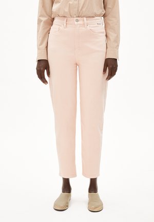 Person trägt hoch taillierte, blass rosa, gerade geschnittene Jeans, ein beiges gestreiftes Hemd mit Knöpfen und beige Slipper vor weißem Hintergrund.