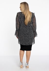 Zwarte en grijze luipaardprint jurk met een doorschijnende overlay, gerimpelde mouwen en een aangesloten zwarte rok, aangevuld met zilveren hoge hakken.