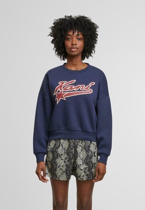 Felpa blu navy con logo a stella rossa e testo vintage, abbinata a pantaloni corti con stampa serpente. Tessuto misto cotone, vestibilità comoda, polsini a coste.