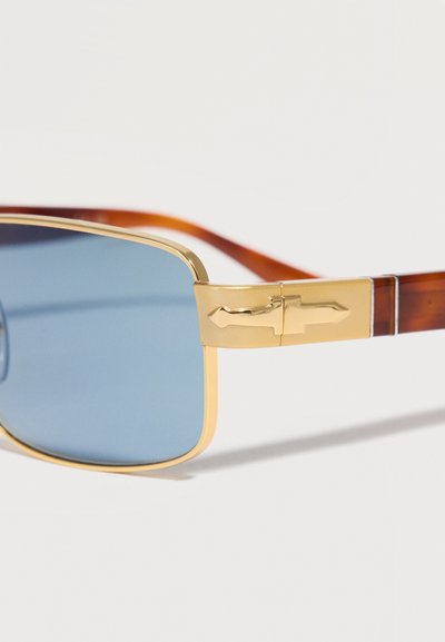 Blåtone rektangulære solbriller med guldfarvet metalstel og skildpaddemønstrede stelarme med en pilformet guld hængseldetalje.
