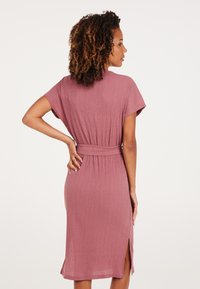 Vestido rosa frambuesa con mangas cortas en forma de murciélago, cintura ceñida con cinturón, abertura lateral y tela texturizada, visto desde la parte de atrás.