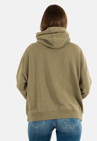 Olijfgroene hoodie met een grote capuchon, ontspannen pasvorm en ribbelzoom. Gecombineerd met klassieke blauwe spijkerbroek met details op de achterzak.