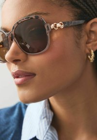 Sonnenbrille mit einem grauen Leopardenmuster-Rahmen, braunen Gläsern und goldenen Akzenten. Eine Nahaufnahme, die die Form und Textur hervorhebt.