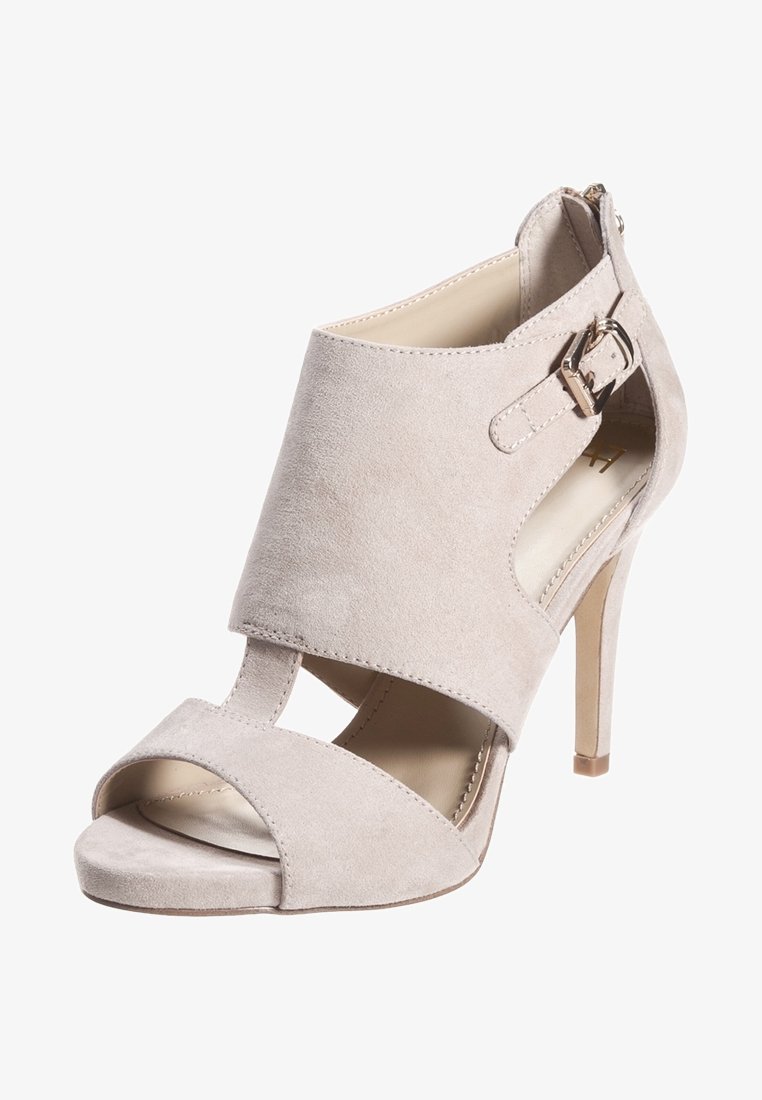 Sandale beige en daim à talon haut avec bout ouvert, côtés découpés et bride de cheville ajustable avec boucle argentée.