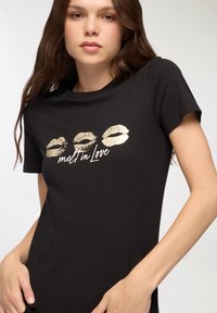 Czarna bawełniana koszulka z nadrukiem złotych ust i napisem "melt in Love". Krótkie rękawy i okrągły dekolt. Gładka tekstura.
