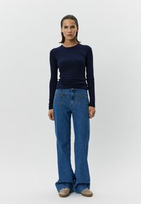 Toppia tummansinistä pitkähihaista paitaa yhdistettynä korkeavyötäröisiin, vaaleansinihin leveälahkeisiin farkkuihin. Farkuissa on takataskut ja rento istuvuus, ja asusteena on beiget kengät.